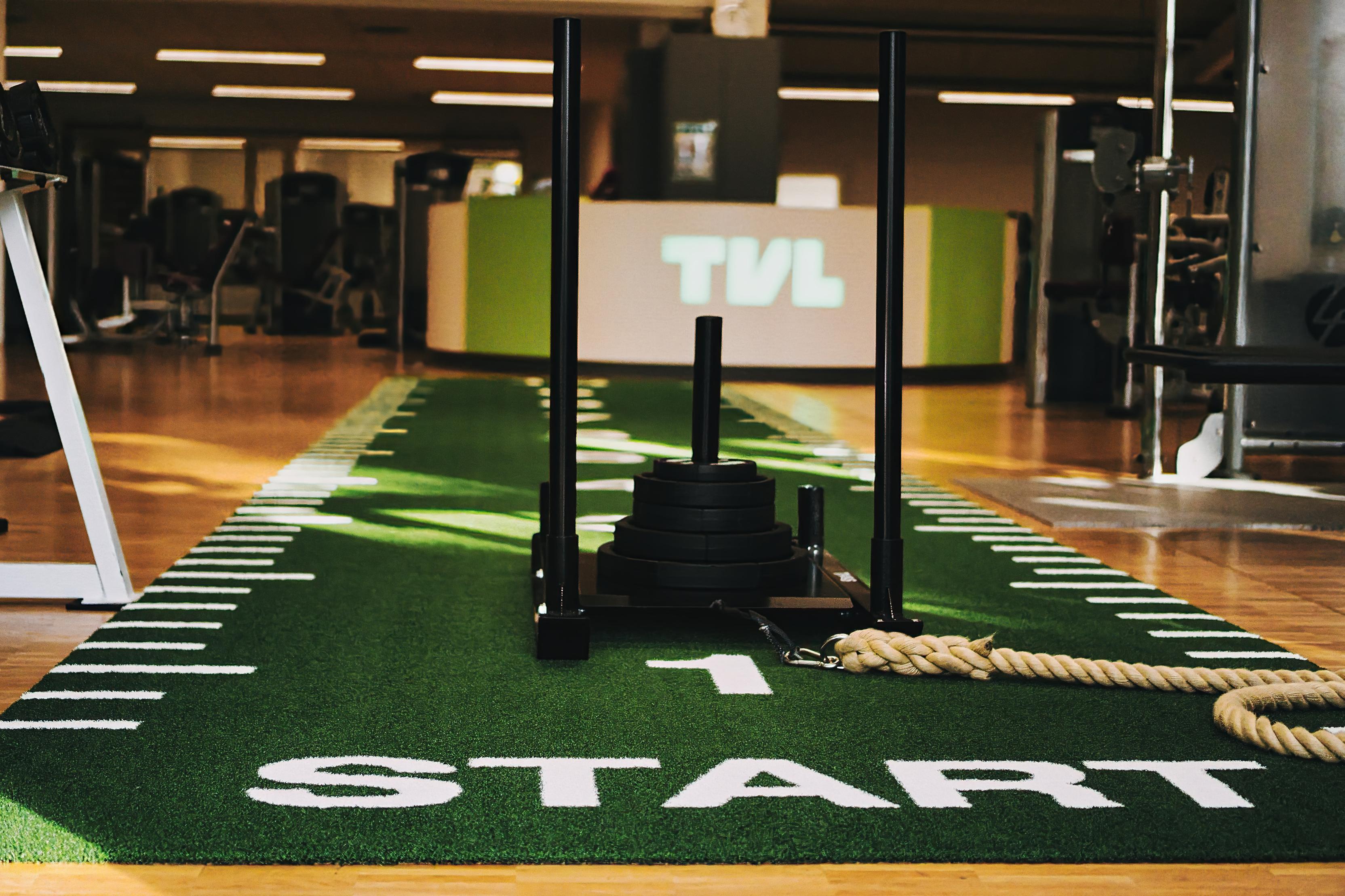 Nahaufnahme einer Fitnesszone mit einem Schlitten, der auf einem grünen Sportboden mit dem Wort "START" liegt.